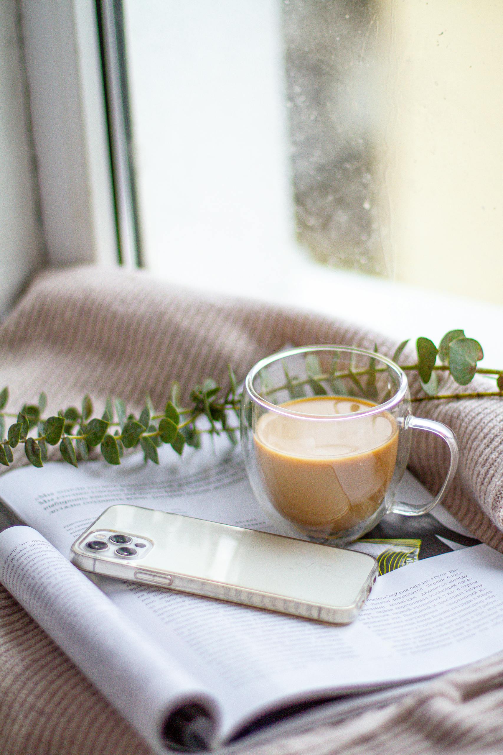 A warm indoor setup featuring a smartphone, coffee, and greenery on a magazine.